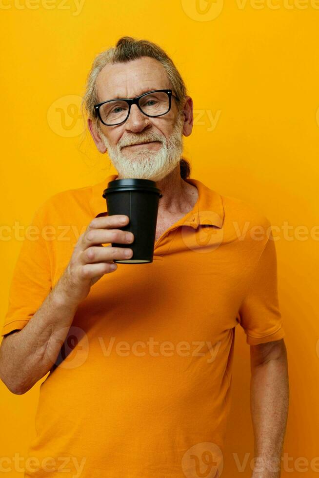 Senior grey-haired man with black disposable cup yellow background photo