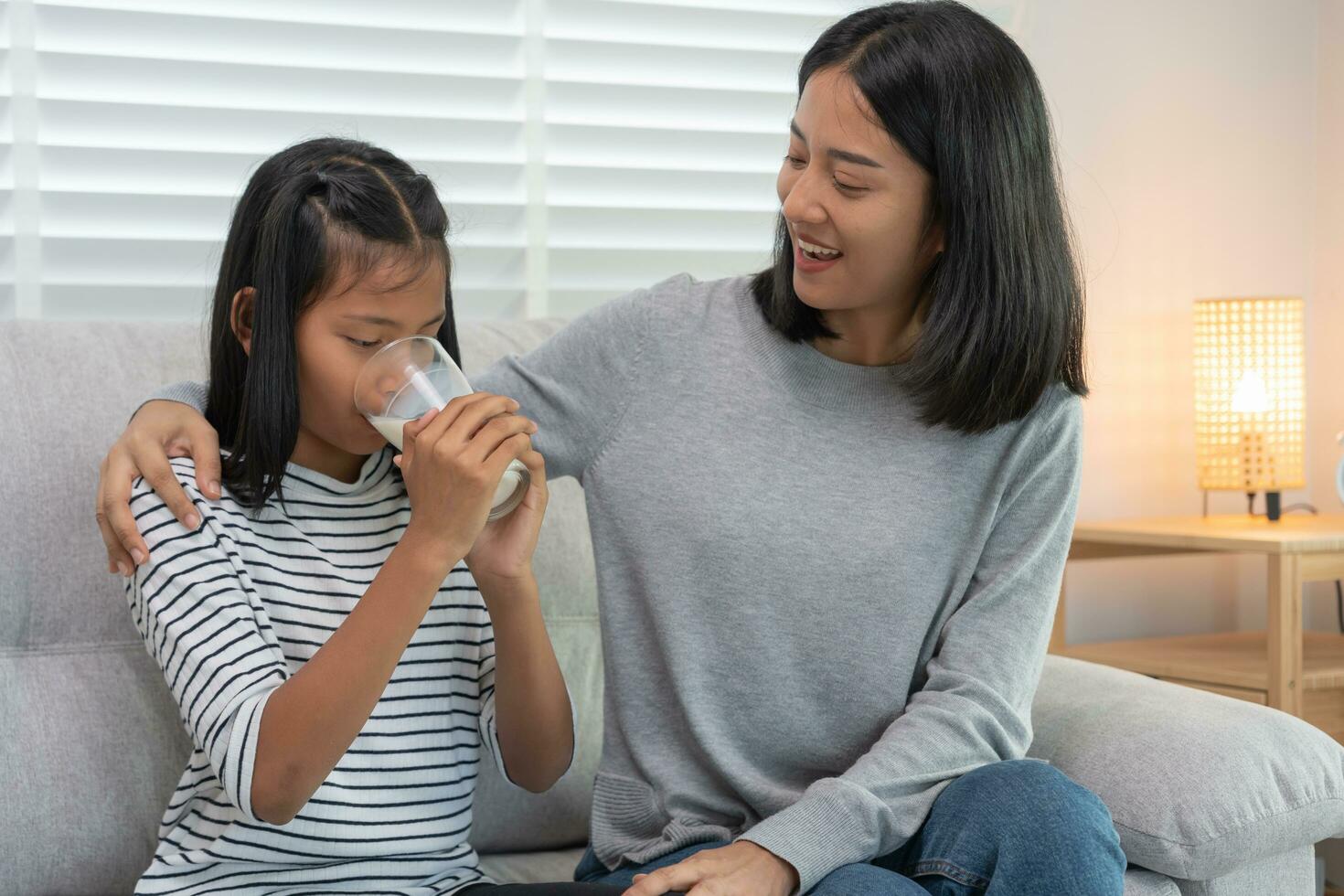 Asian young little girl learn at home. Do homework with kind mother help, encourage for exam. Mom pass on a glass of milk to daughter. Girl happy Homeschool. Mom teach and advice education together. photo