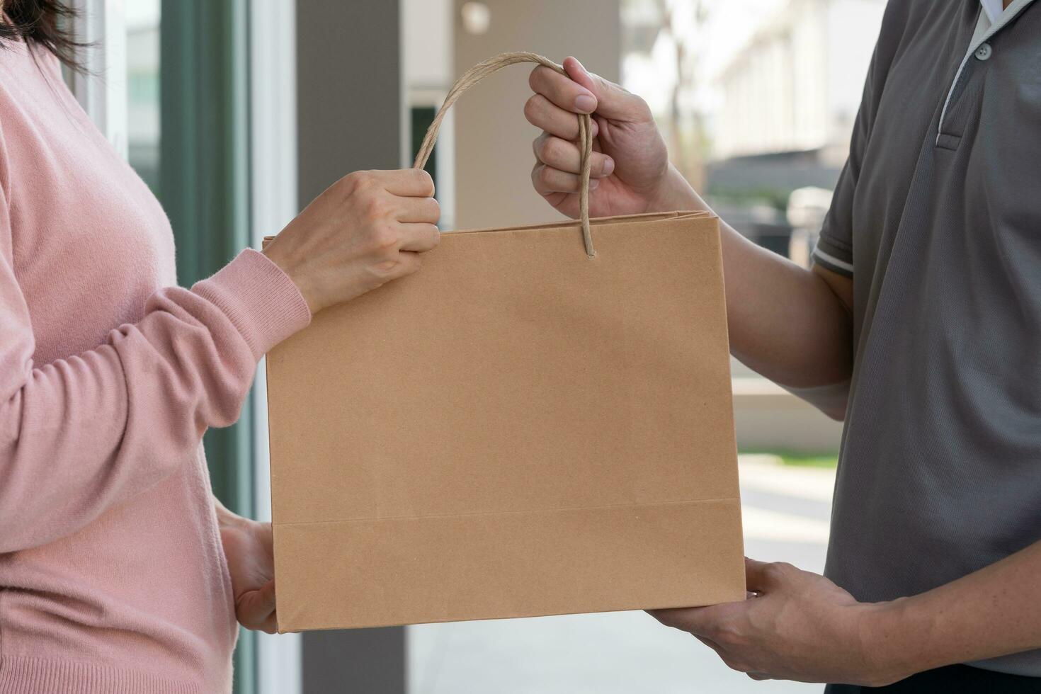 Happy smiling Asian woman receives paper bag parcel of food from courier front house. Delivery man send deliver express. online shopping, paper container, takeaway, postman, delivery service, packages photo