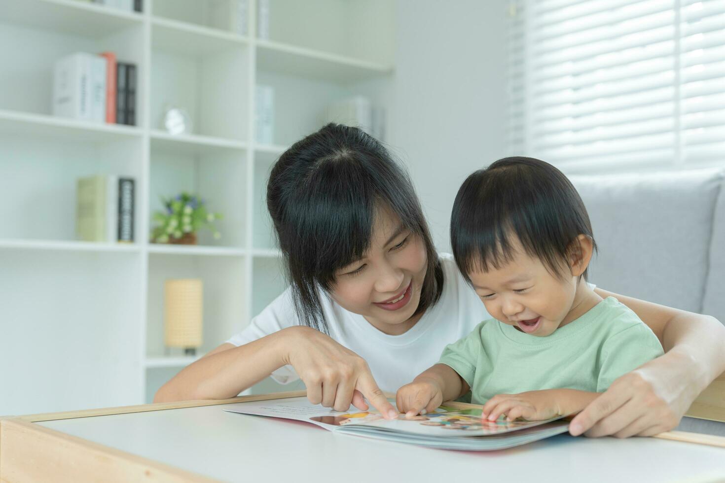 Happy Asian mother relax and read book with baby time together at home. parent sit on sofa with daughter and reading a story. learn development, childcare, laughing, education, storytelling, practice. photo