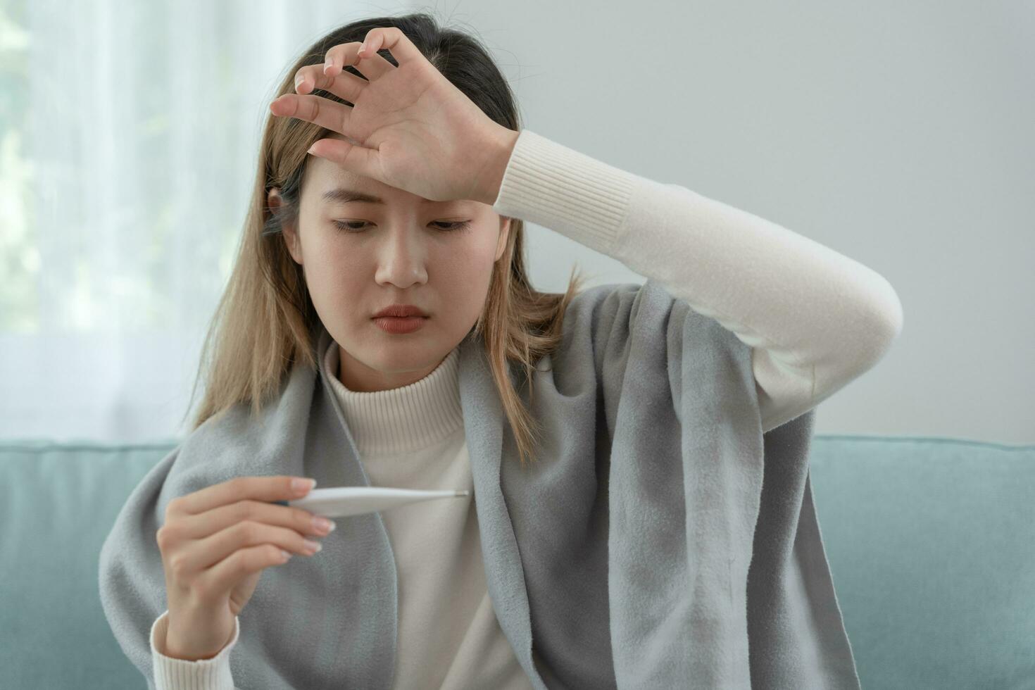 Young Asian woman having high fever while checking body temperature, female sneezing and runny nose with seasonal influenza, allergic, digital thermometer, virus, coronavirus, illness, respiratory photo