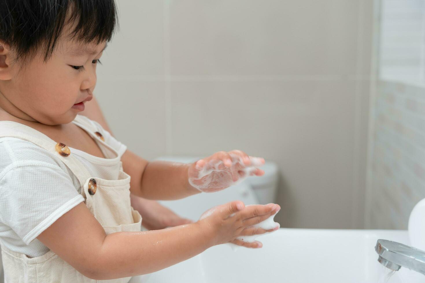 pequeño niño manos lavar con jabón burbujas y enjuague con limpiar agua a evitar y detener el untado de gérmenes después espalda a hogar, virus o COVID-19. bueno salud y bueno personal higiene, virus, bacterias foto
