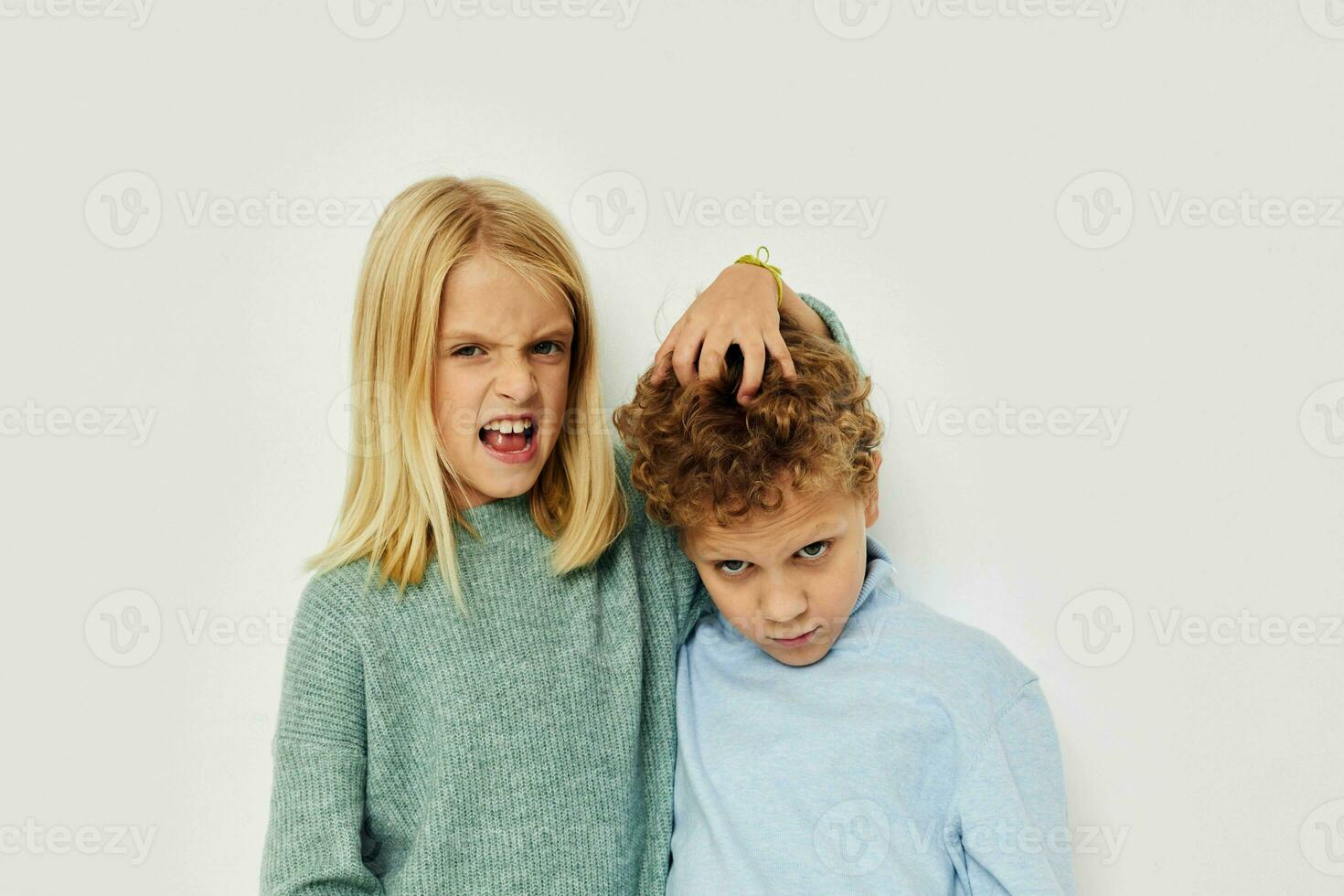 Photo of two children in multi-colored sweaters posing for fun light background