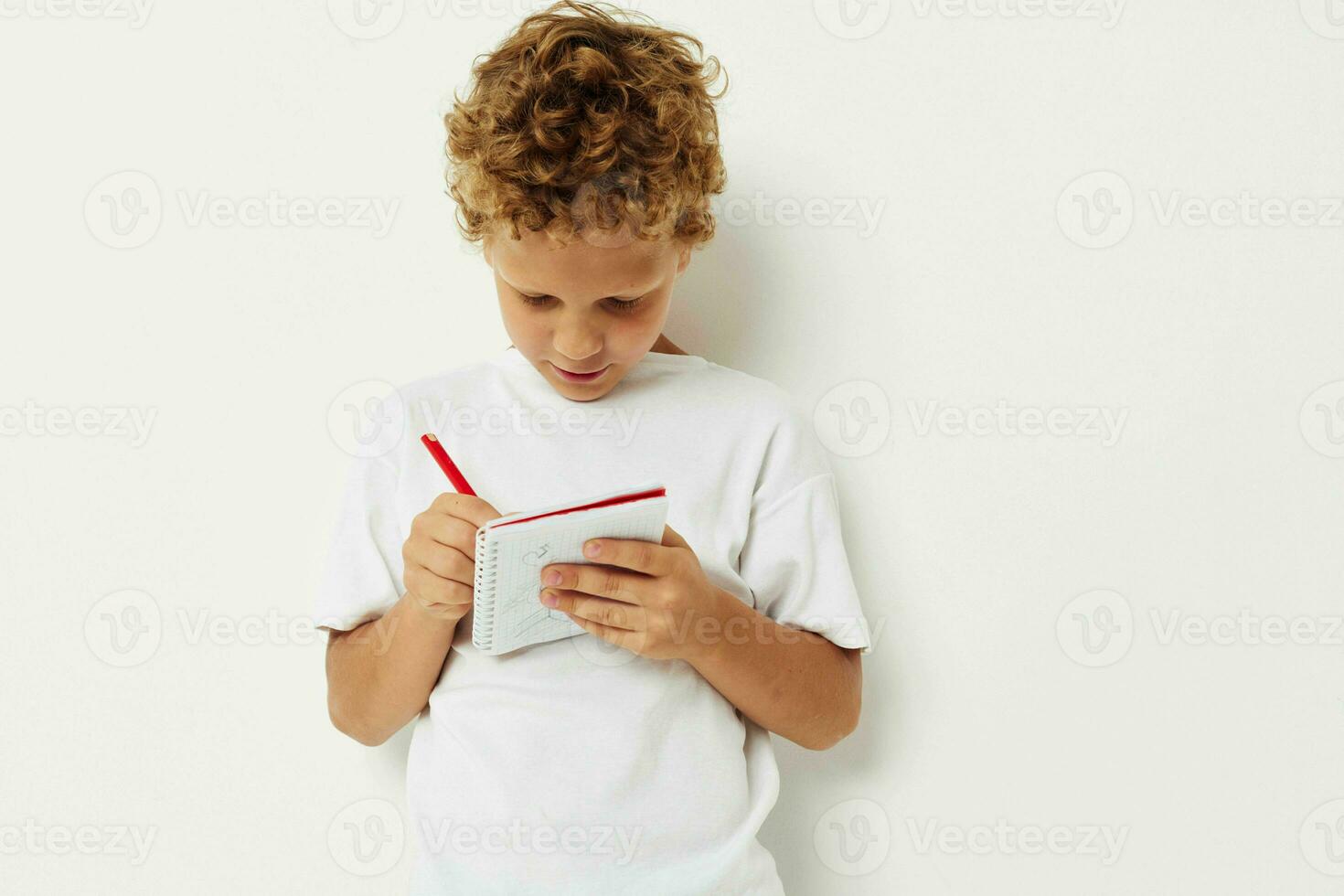 A cheerful boy with curly hair draws in a notebook with a pencil photo