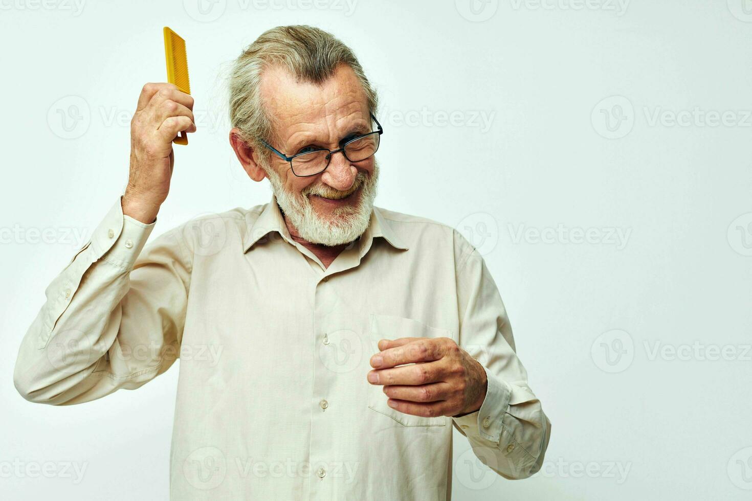 Elderly man combing his hair with a yellow comb in the studio on a gray background photo