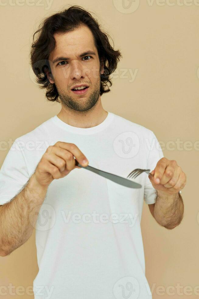 atractivo hombre en un blanco camiseta con cuchillo con tenedor aislado antecedentes foto