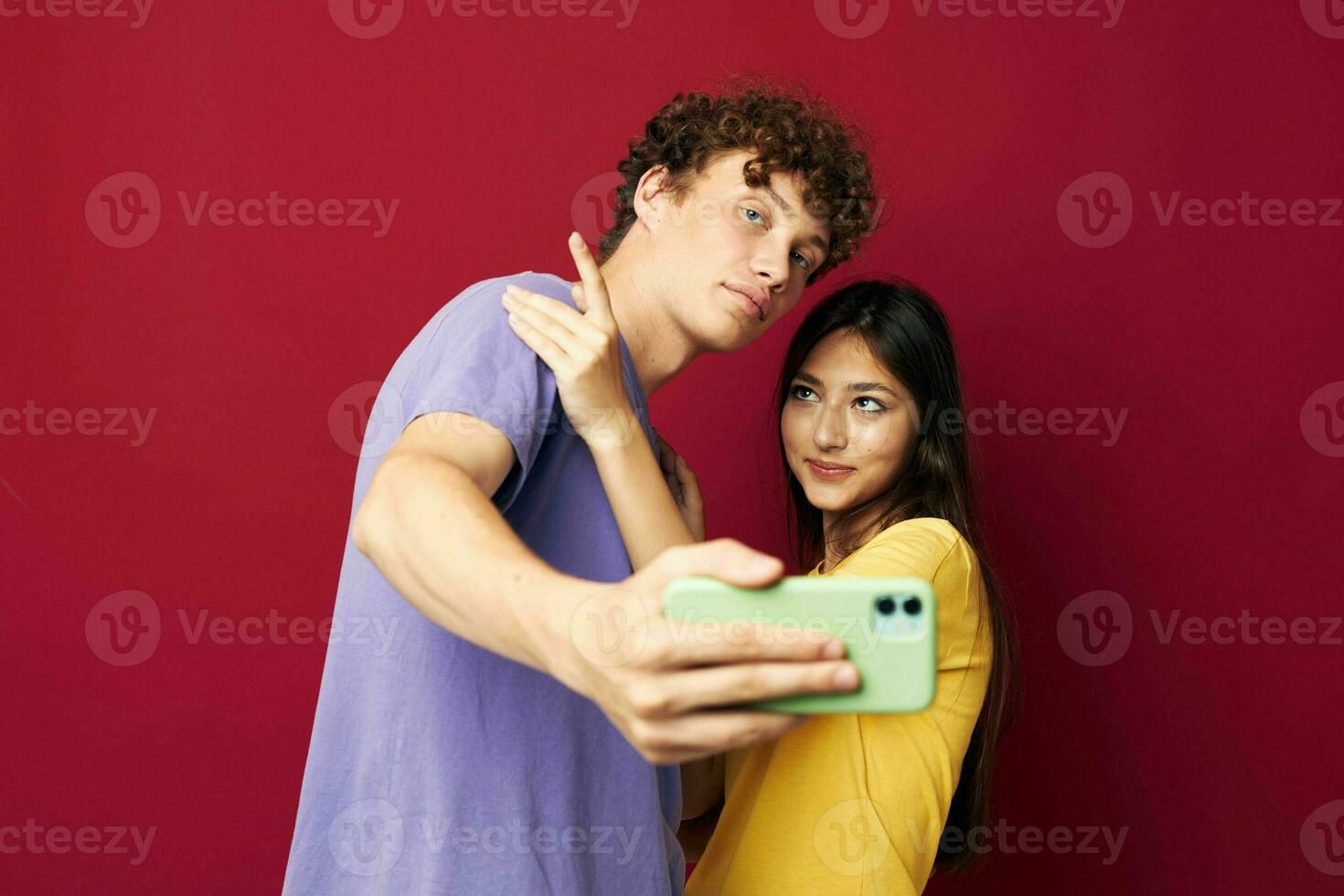 young man and girl in colorful T-shirts with a phone red background photo