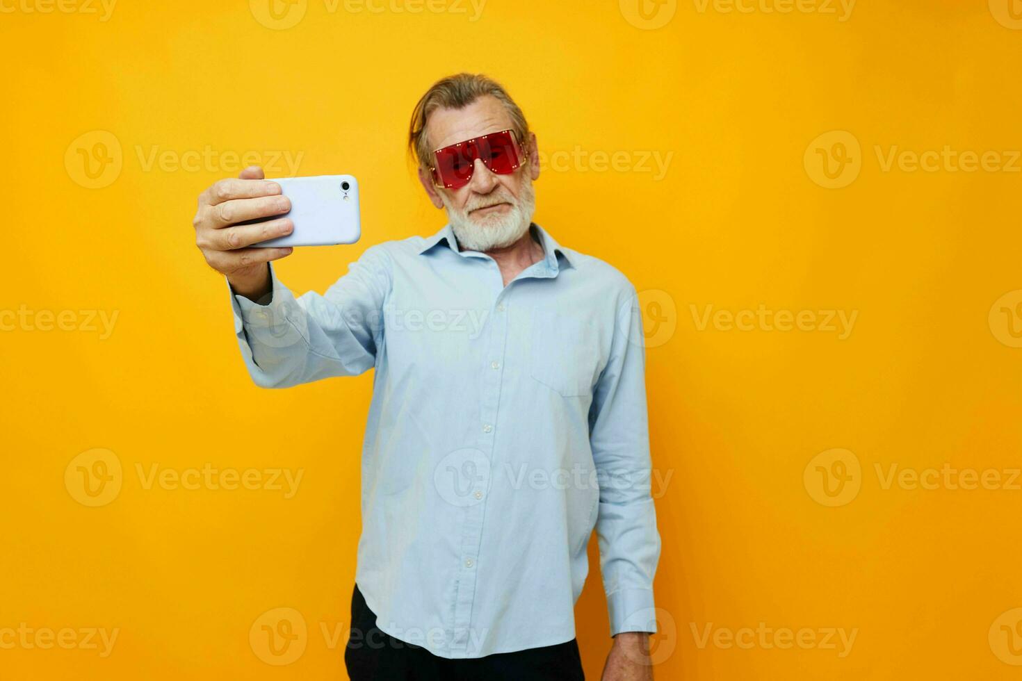 old man in fashionable red glasses with a phone yellow background photo