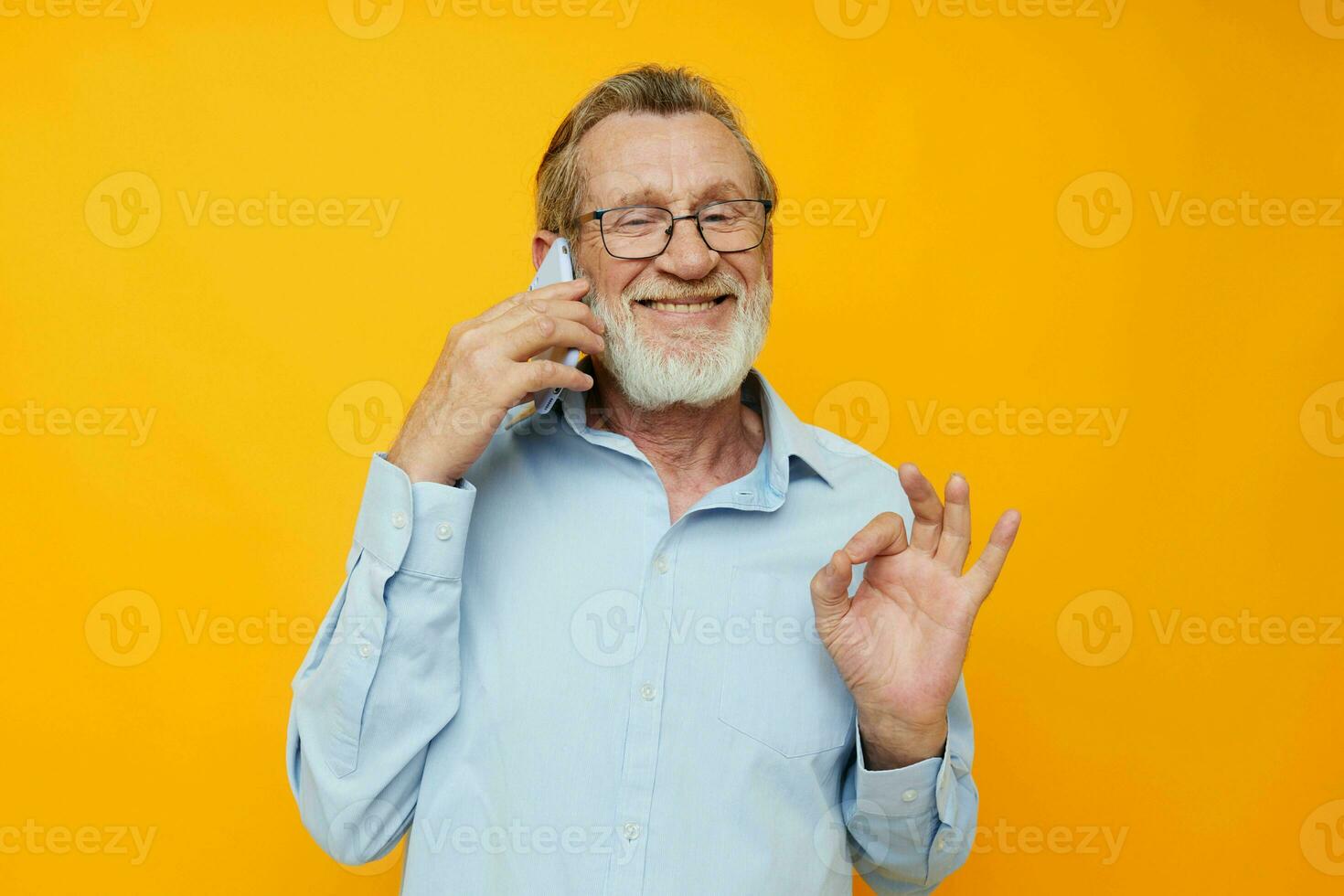 Senior grey-haired man talking on the phone posing close-up yellow background photo