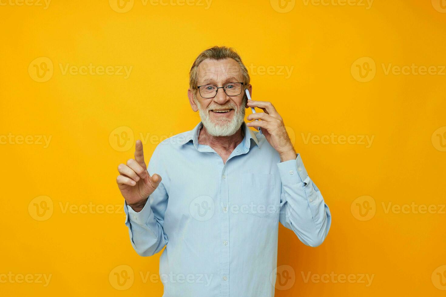 old man in a blue shirt and glasses talking on the phone yellow background photo