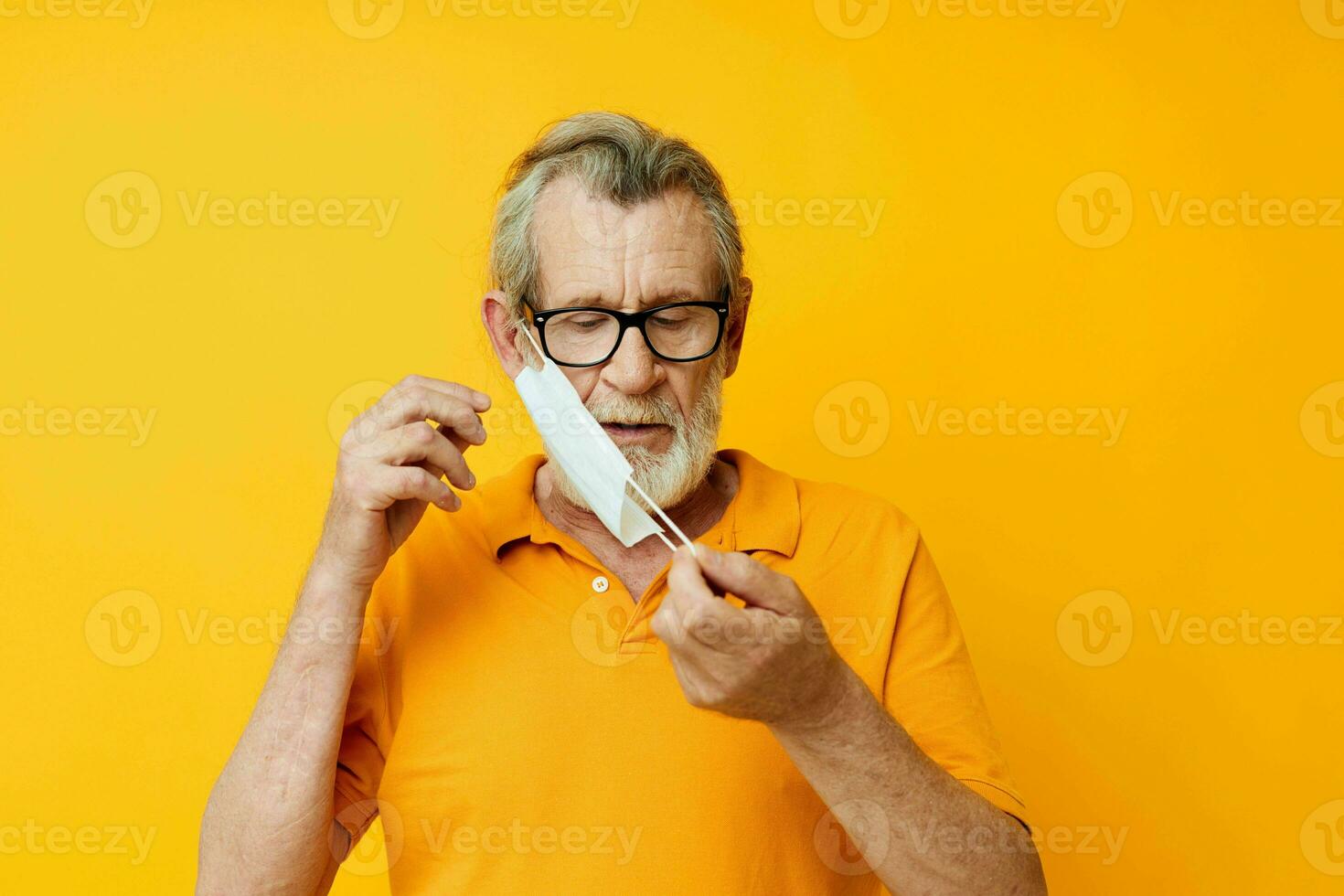 Photo of retired old man medical mask in a yellow shirt isolated background