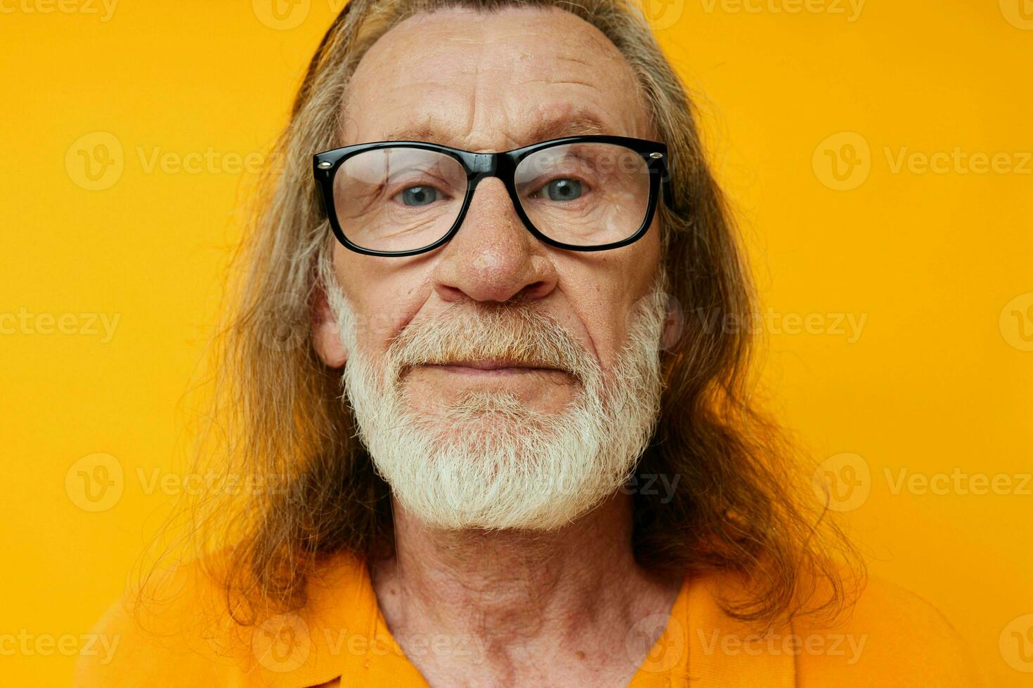 Gray-haired elderly man with a beard wearing glasses close up yellow background photo
