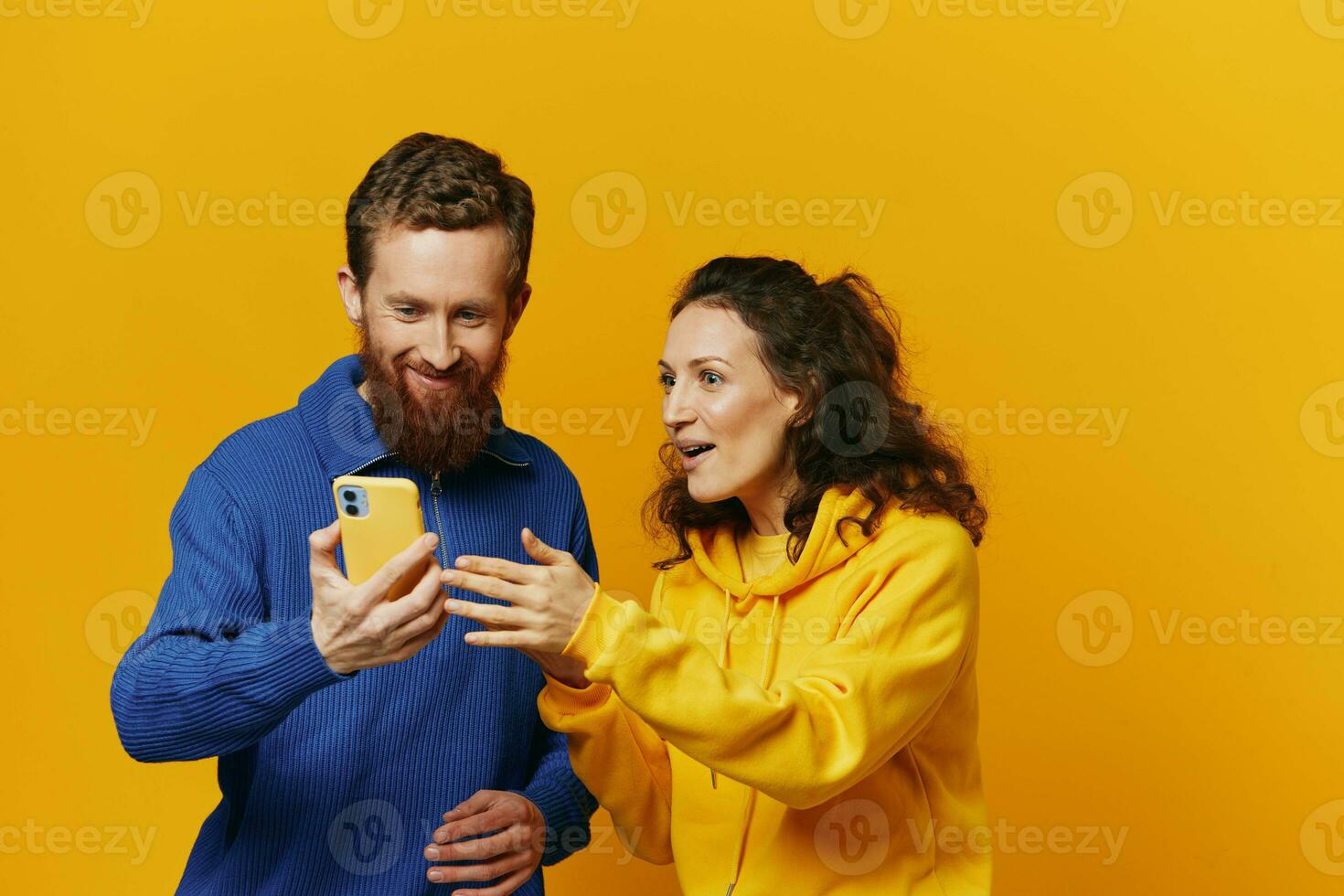 Man and woman couple smiling merrily with phone in hand social media viewing photos and videos, on yellow background, symbols signs and hand gestures, family freelancers.