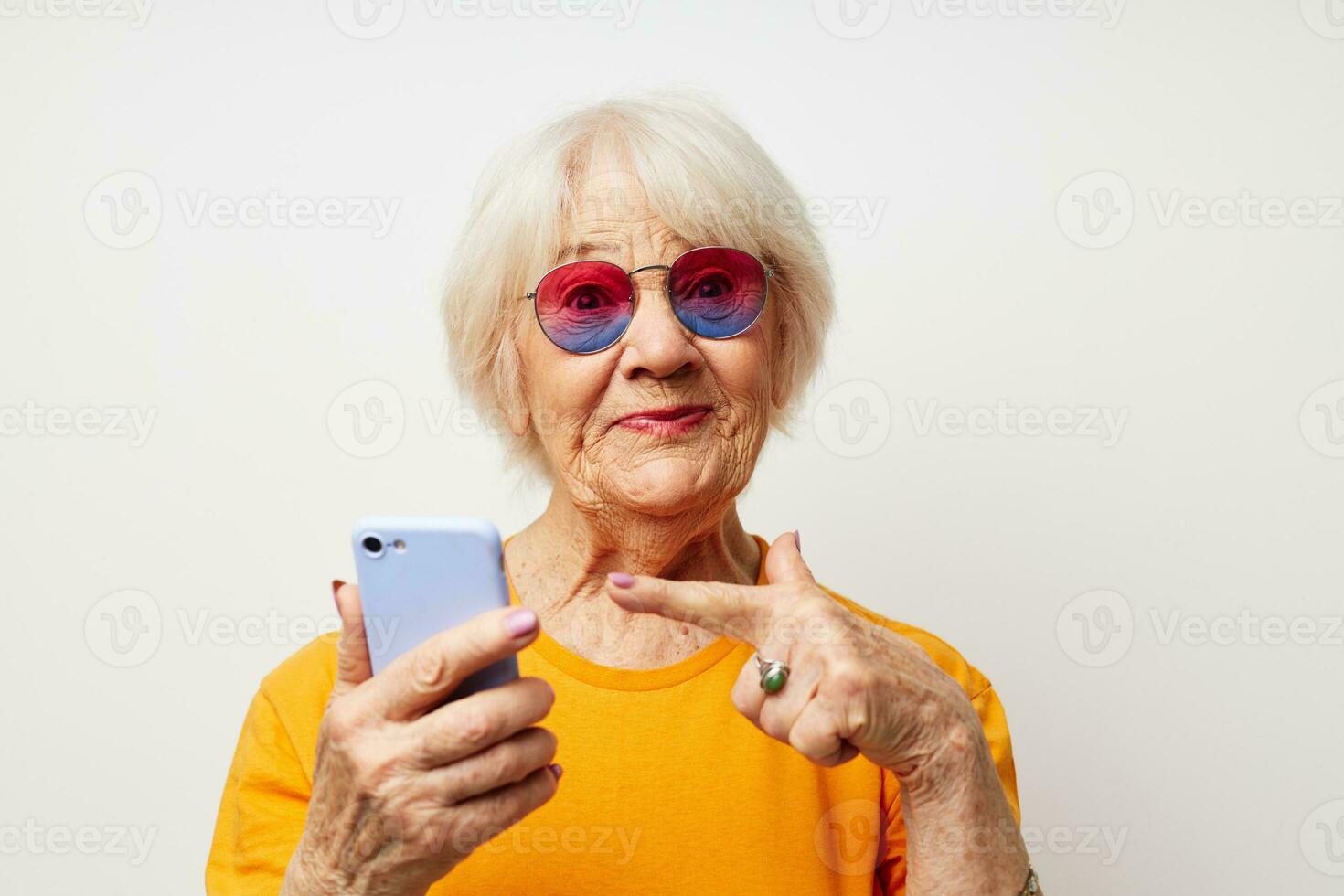smiling elderly woman in fashionable glasses with a smartphone in hand light background photo