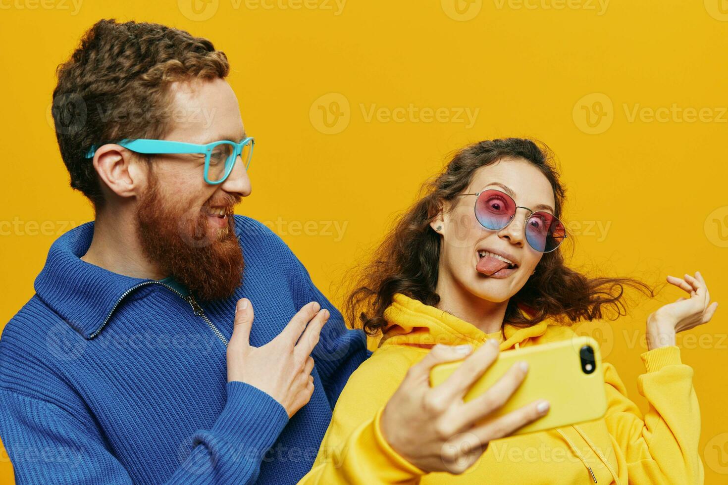 Woman and man funny couple with phones hand social networking and communication crooked do selfies smile fun, on yellow background. The concept of real family relationships, freelancers, work online. photo