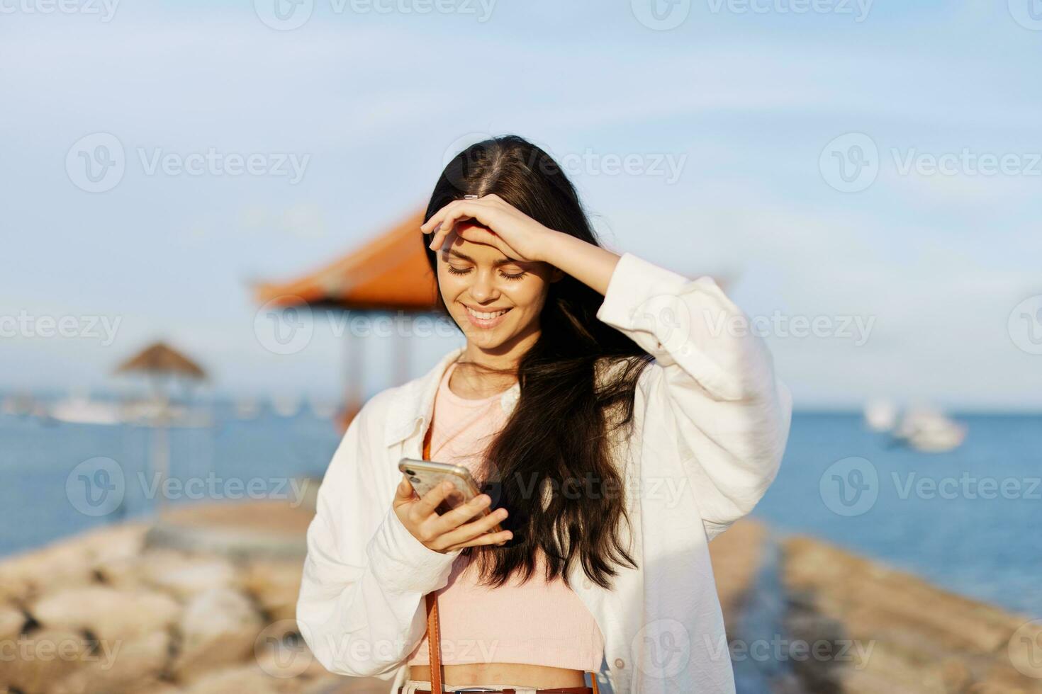 Woman smile blogger freelancer with phone in hand on vacation walking on the beach by the ocean in Bali sunset, happy travel and vacation, mobile communication, internet online photo