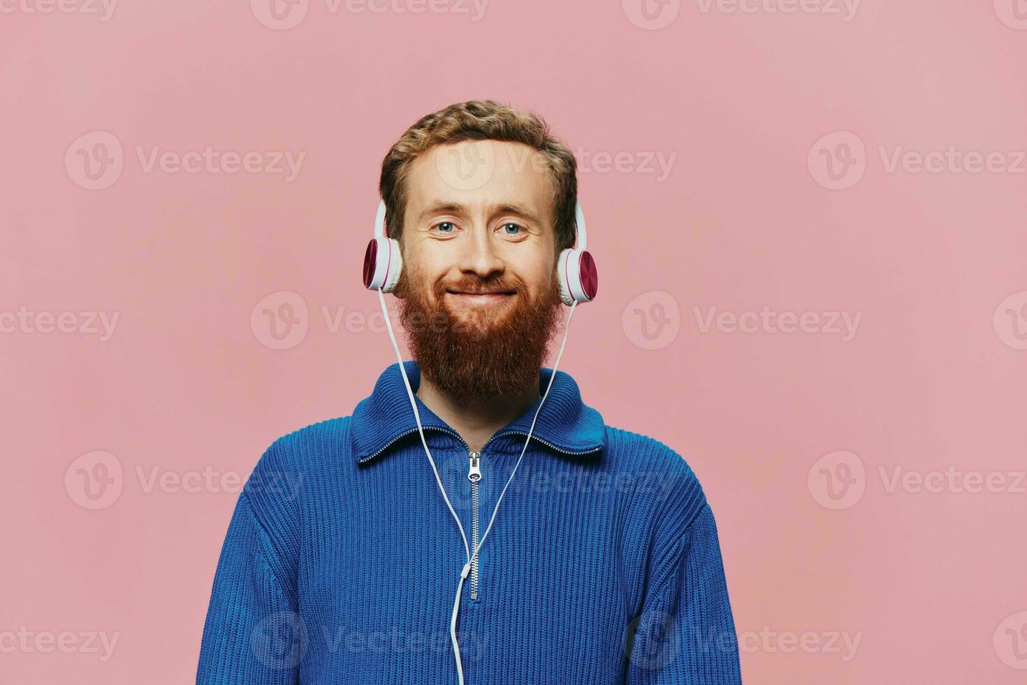 retrato de un pelirrojo hombre vistiendo auriculares sonriente y baile, escuchando a música en un rosado antecedentes. un hipster con un barba. foto