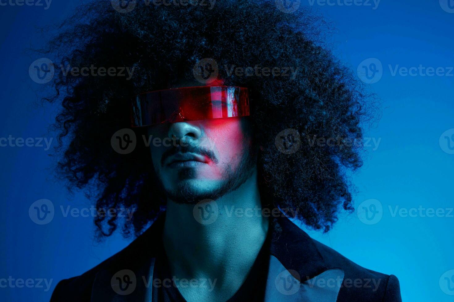 Fashion portrait of a man with curly hair on a blue background wearing red sunglasses, multinational, colored light, trendy, modern concept. photo