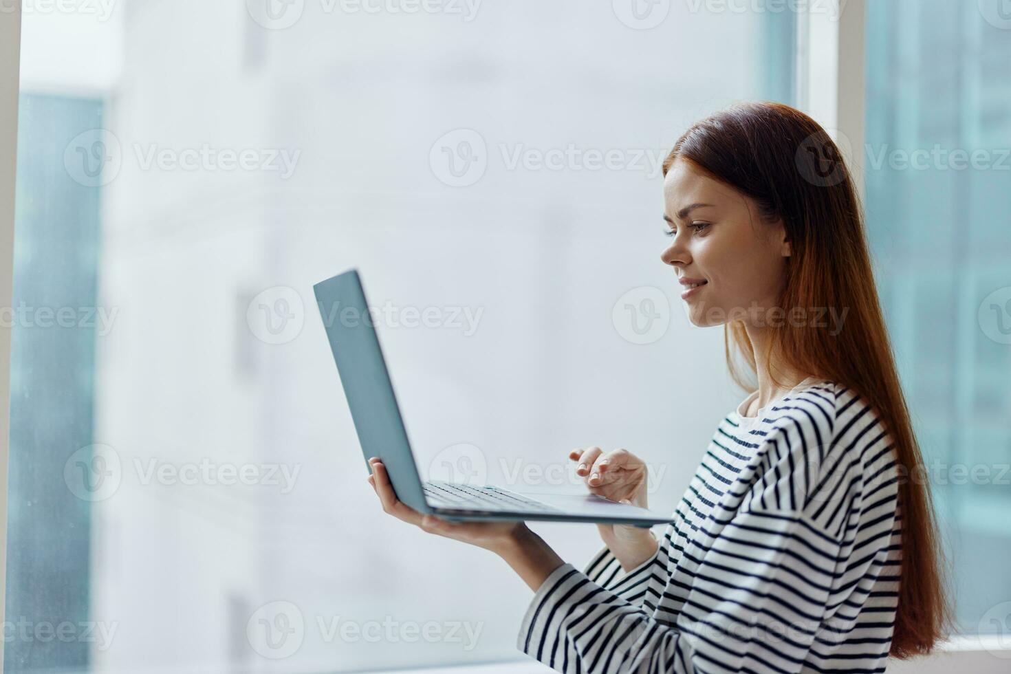 Woman student studying in the city near a window and holding a laptop, working with technology online, smiling photo