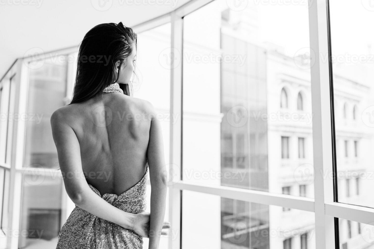 Woman in gold sequined dress by the window poses in a stylish image designer dress with open back, party look black and white photo