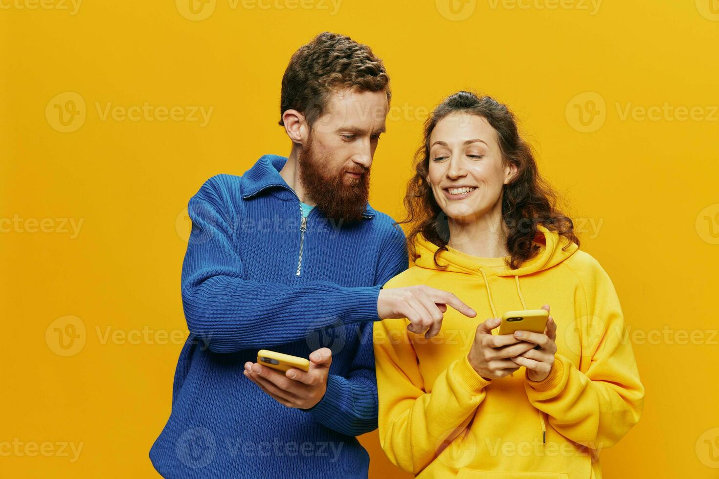 Woman man cheerful couple with phones in hand social networking and communication crooked smile fun and fight, in yellow background. The concept of real family relationships, freelancers, work online. photo