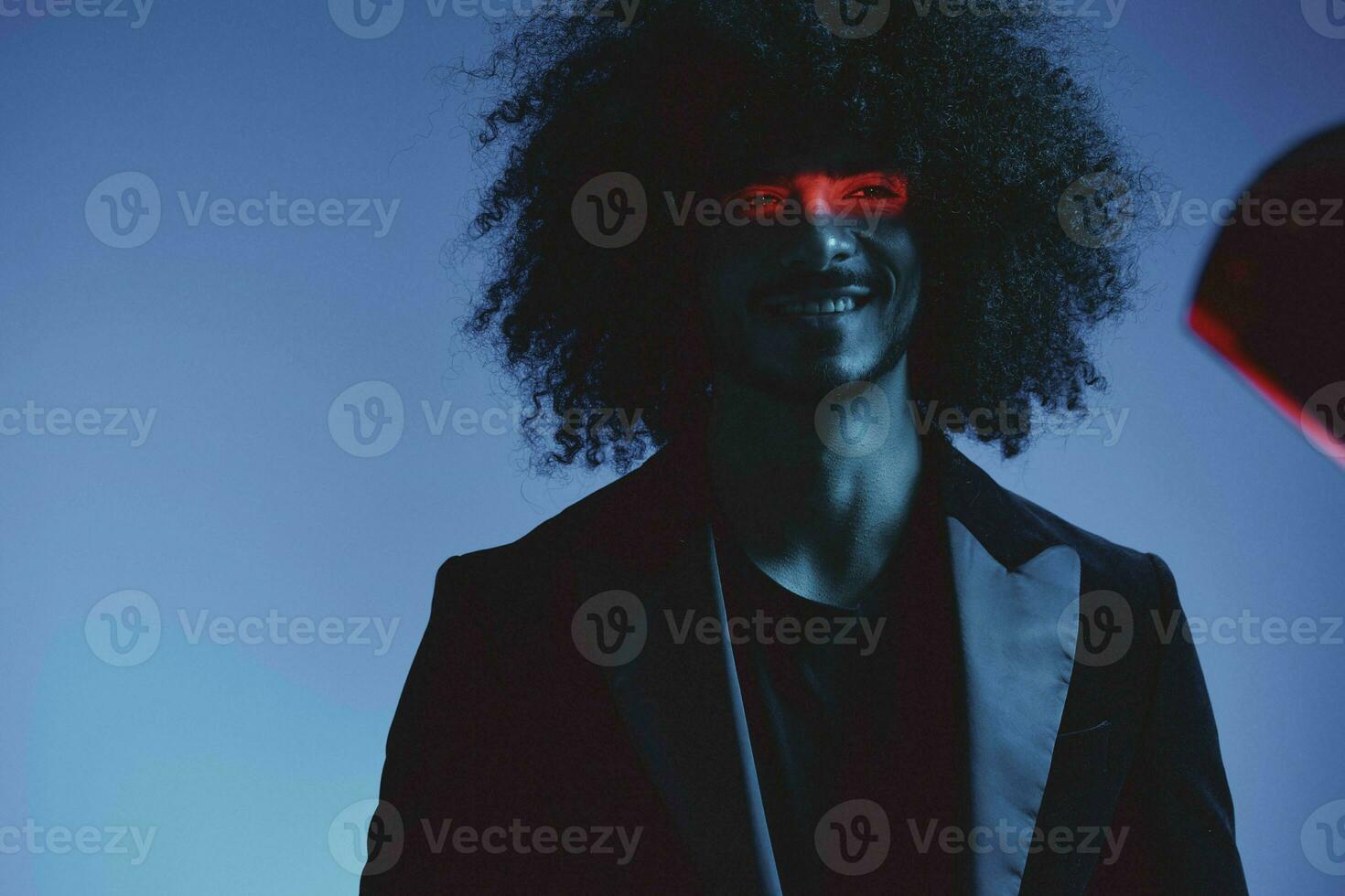 Fashion portrait of a man with curly hair on a blue background with a red stripe of light, multicolored light, trendy, modern concept. photo