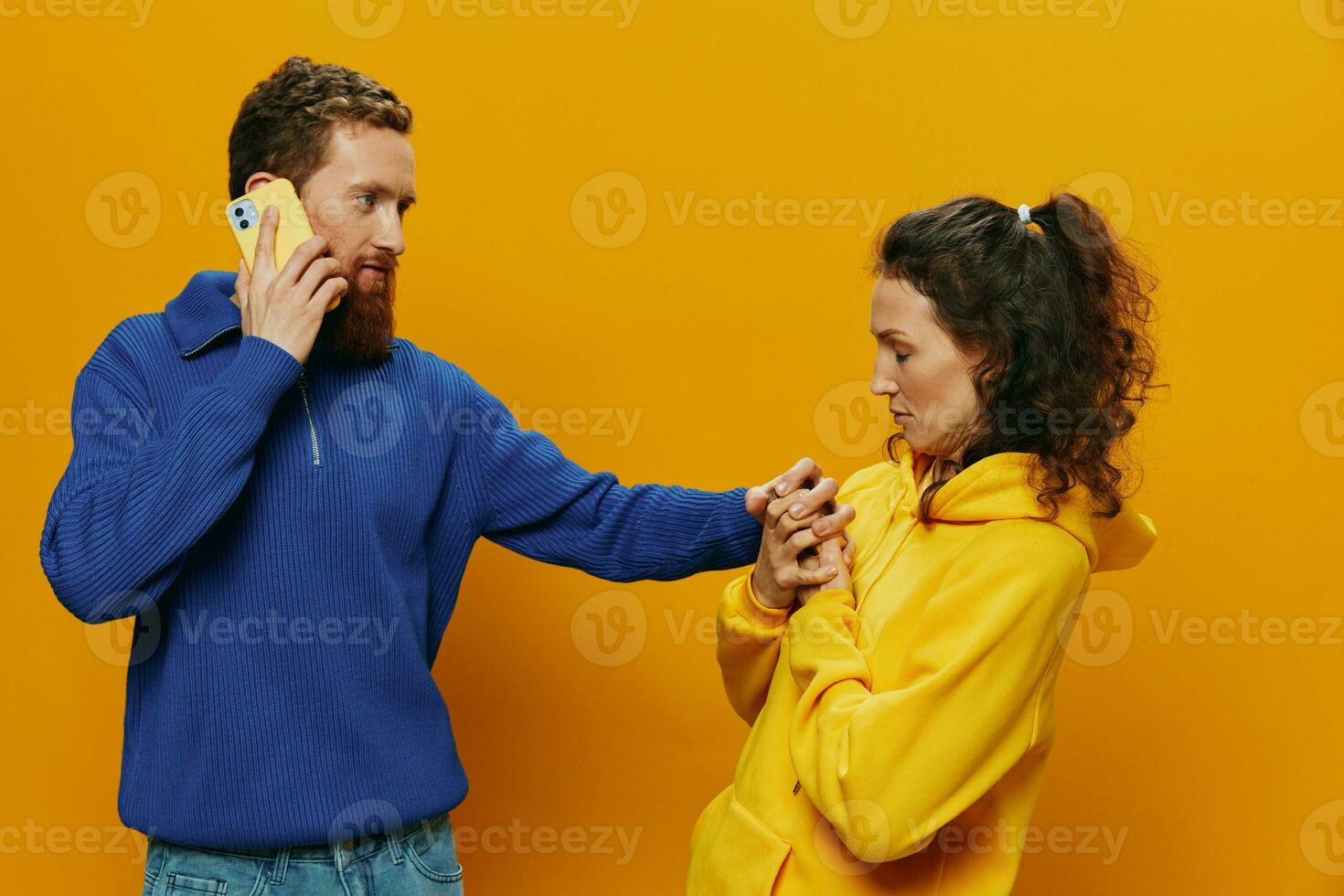 Woman man cheerful couple with phones in hand social networking and communication crooked smile fun and fight, in yellow background. The concept of real family relationships, freelancers, work online. photo