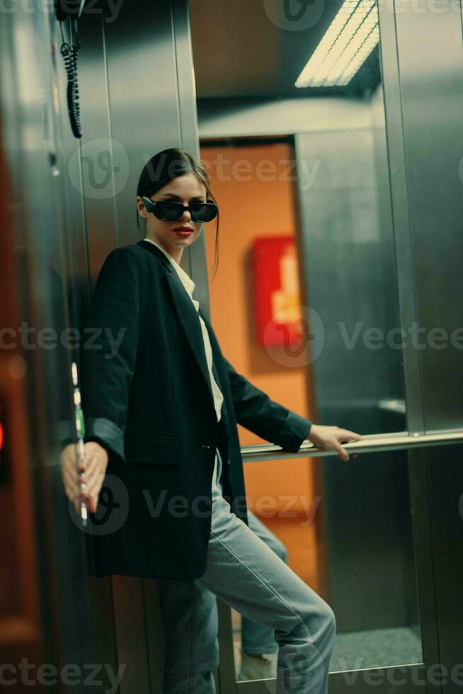 Stylish woman in black jacket and sunglasses posing in elevator, fashion model, dark cinematic light and color photo