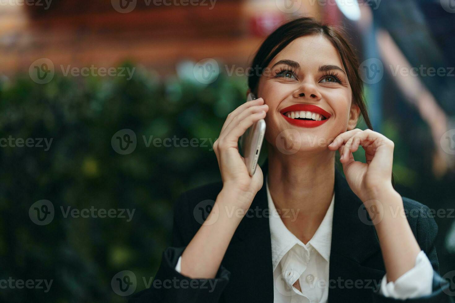 Woman blogger tourist sits in a cafe at a table with a phone in her hands conversation, mobile communication and internet in spring travel, video business call, freelance work online, smile with teeth photo