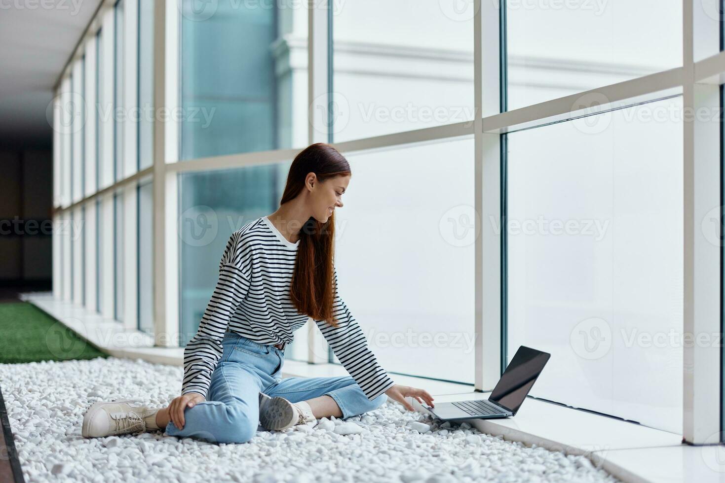 A woman freelancer sits in the office lobby by the big windows and works on her laptop online via the Internet, freelance work anywhere in the world photo