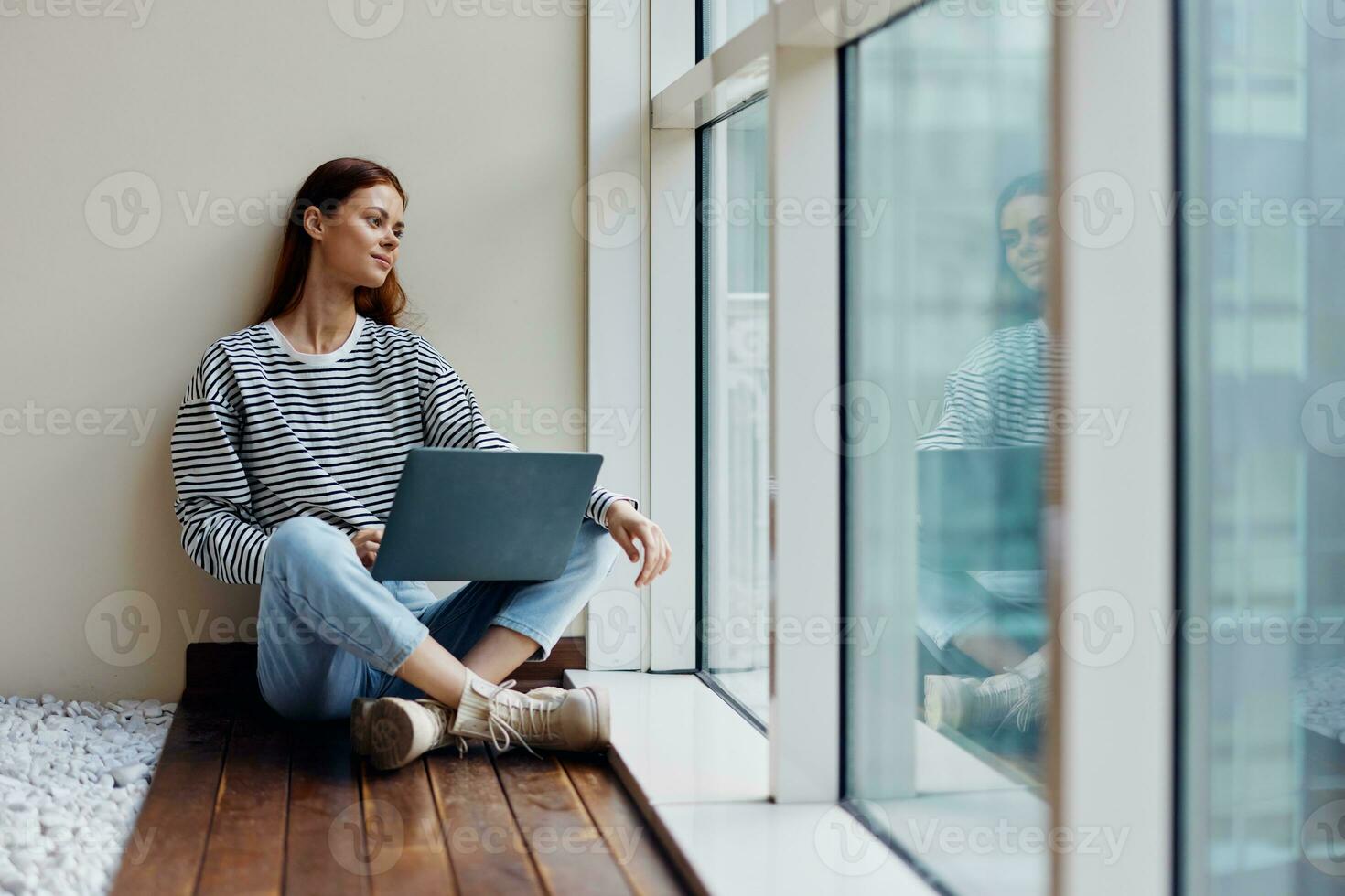 Business woman sitting with a laptop at the window full-length and smiling and looking out the window, happy woman work online in the office, copy space photo