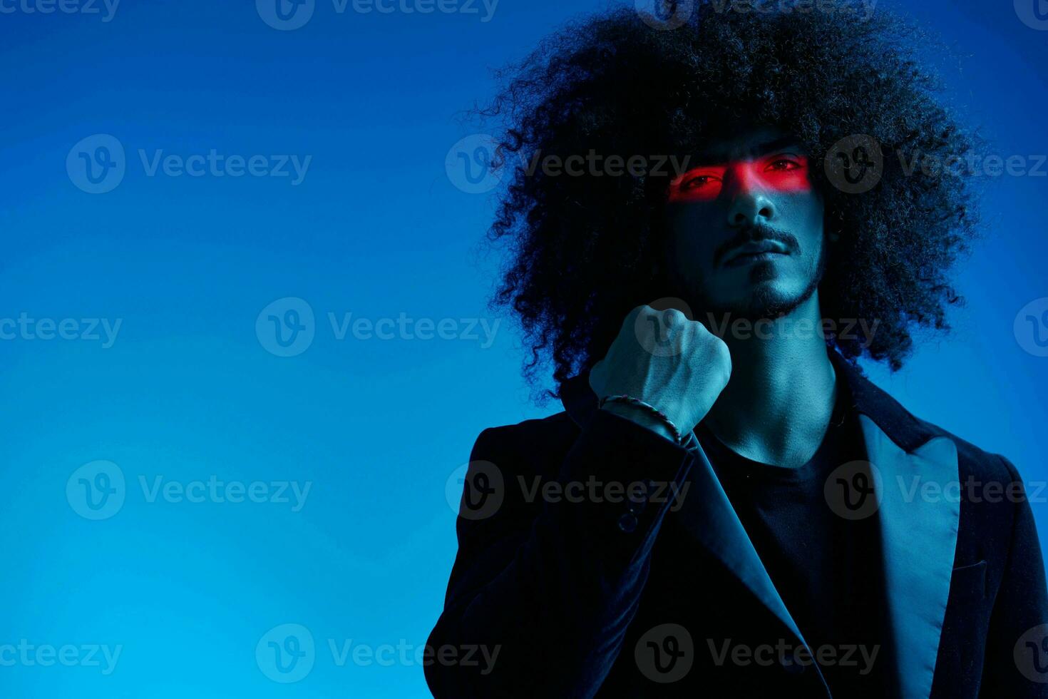 Fashion portrait of a man with curly hair on a blue background with a red stripe of light, multicolored light, trendy, modern concept. photo