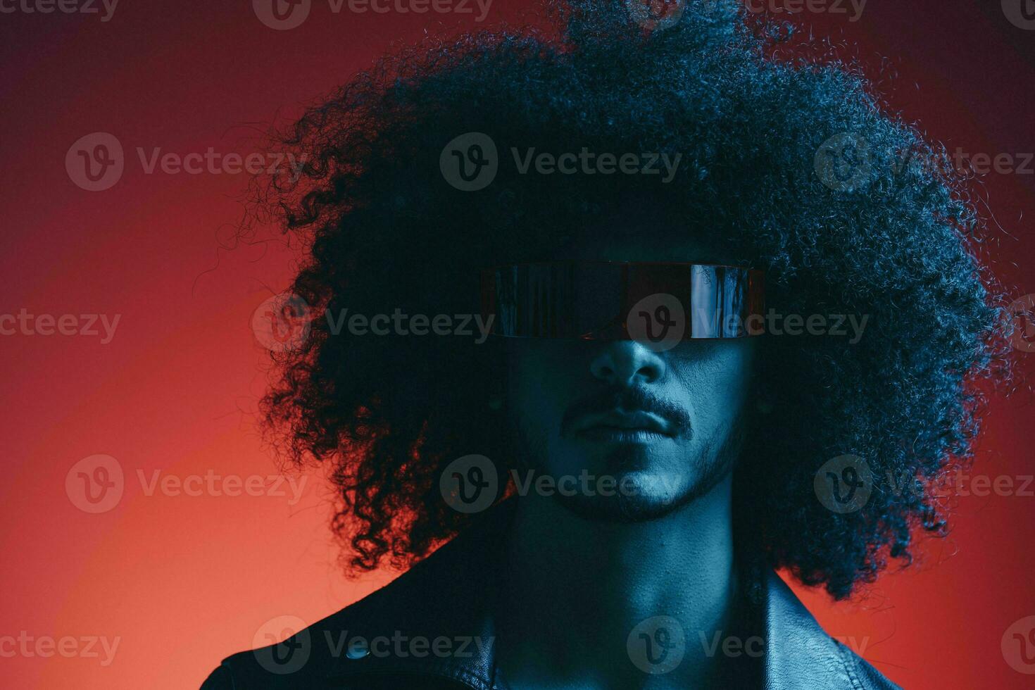 Portrait of fashion man with curly hair on red background with stylish glasses, multicultural, colored light, black leather jacket trend, modern concept. photo