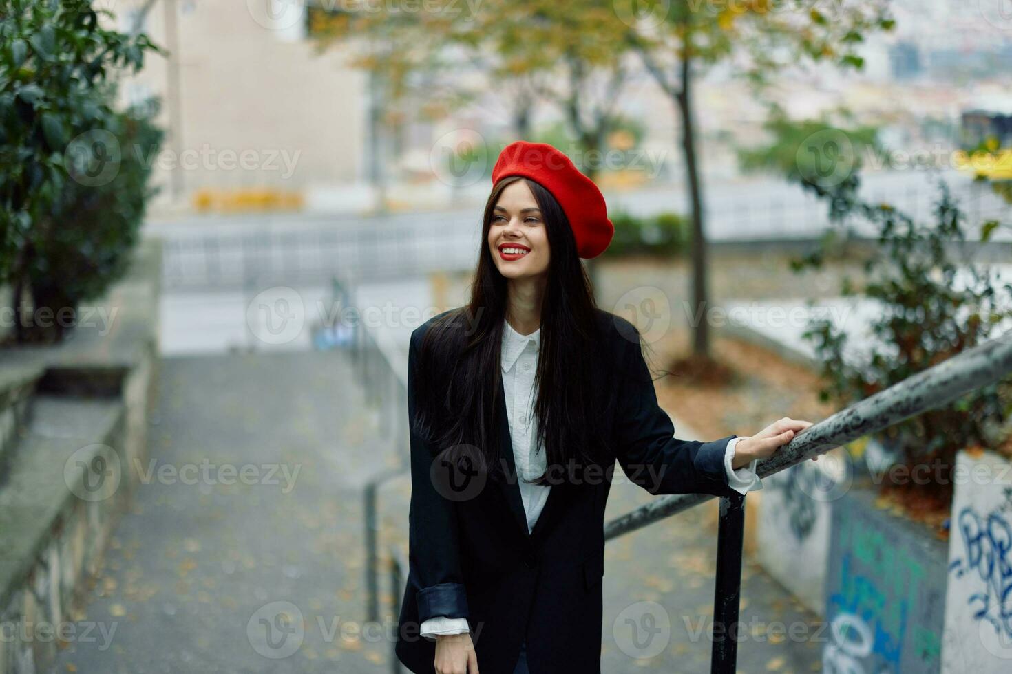 Moda mujer caminando abajo pasos en contra ciudad fondo en elegante ropa con rojo labios y rojo boina, viajar, cinematográfico color, retro Clásico estilo, urbano Moda estilo de vida. foto