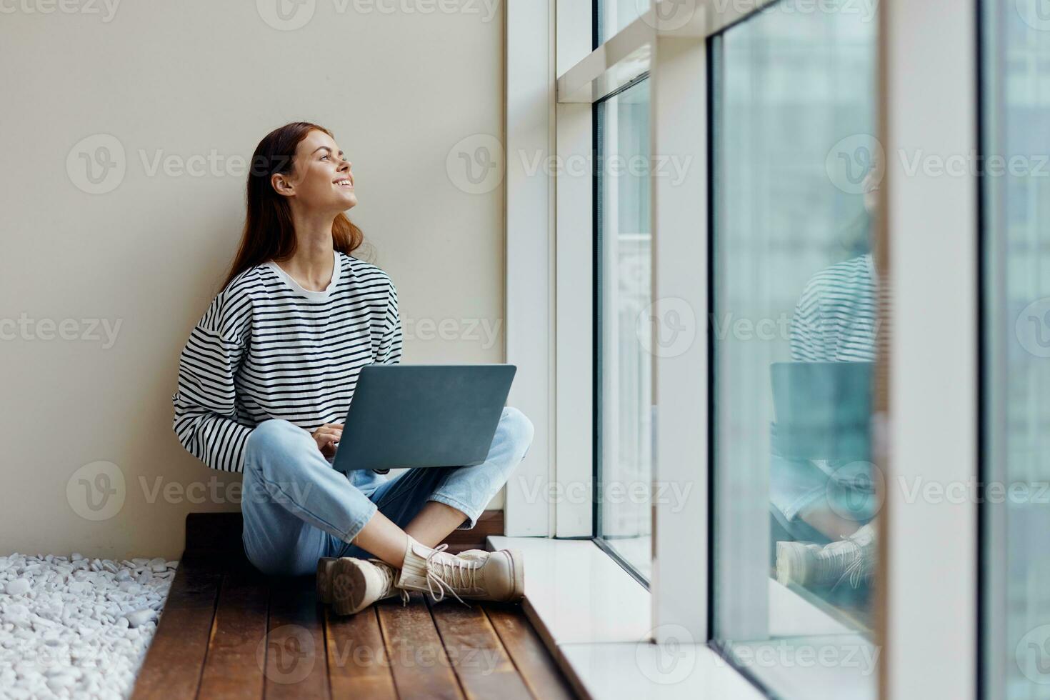 Business woman sitting with a laptop at the window full-length and smiling with teeth and looking out the window, happy woman work online in the office, copy place photo