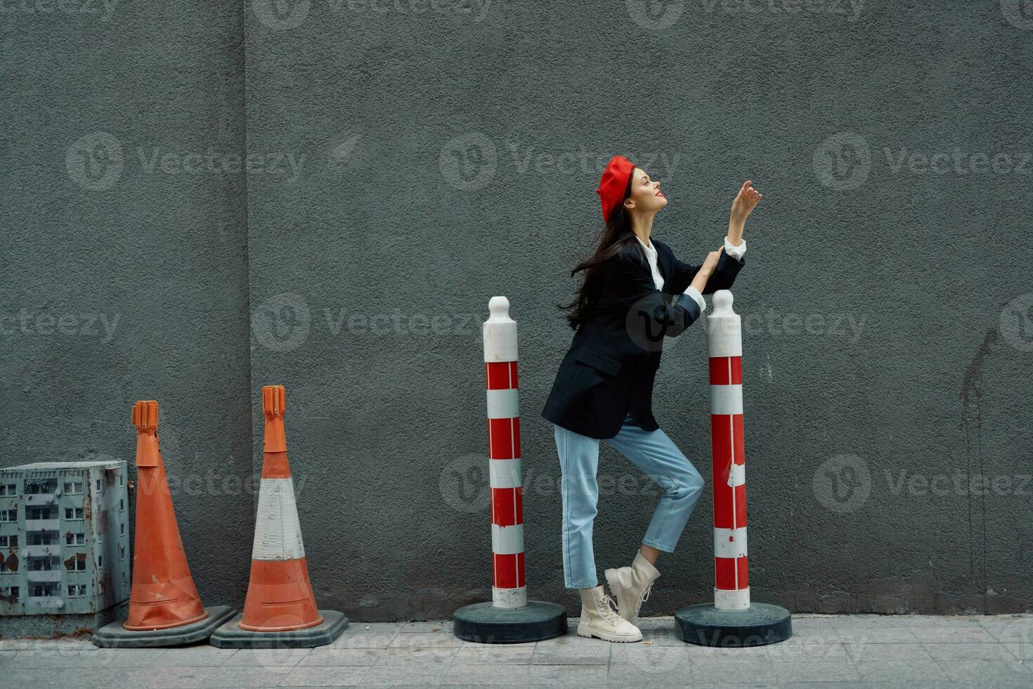 Moda mujer en pie propensión en contra un pared calle en contra un antecedentes de el ciudad la carretera trabajos turista en elegante ropa con rojo labios y rojo boina, viajar, cinematográfico color, retro Clásico estilo. foto