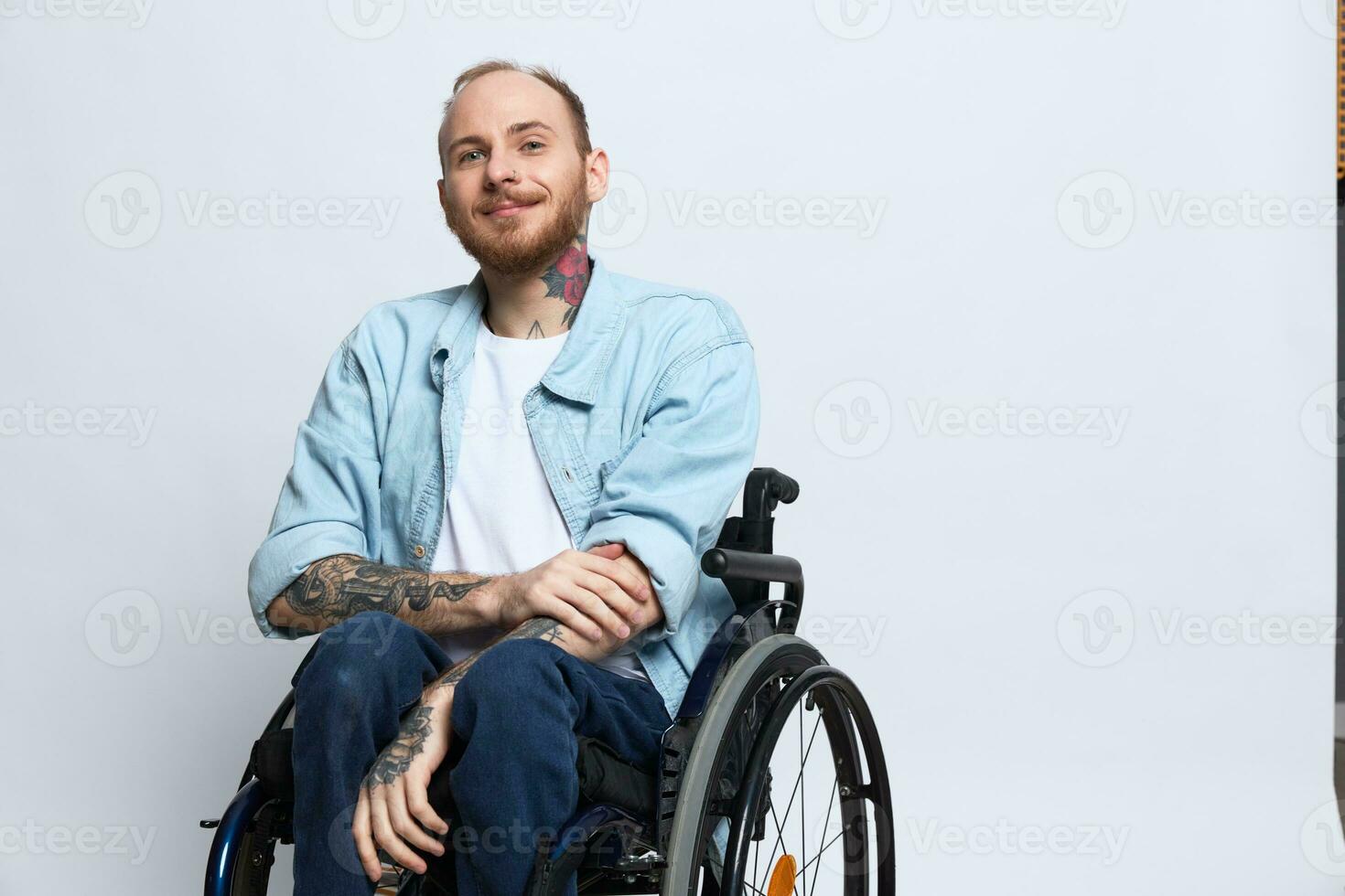 A man in a wheelchair smile, copy space, with tattoos on his arms sits on a gray studio background, the concept of health is a person with disabilities, a real person photo