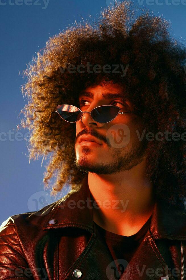 Portrait of a stylish man with curly hair on a blue background multinational, colored light, trendy glasses, modern concept. photo