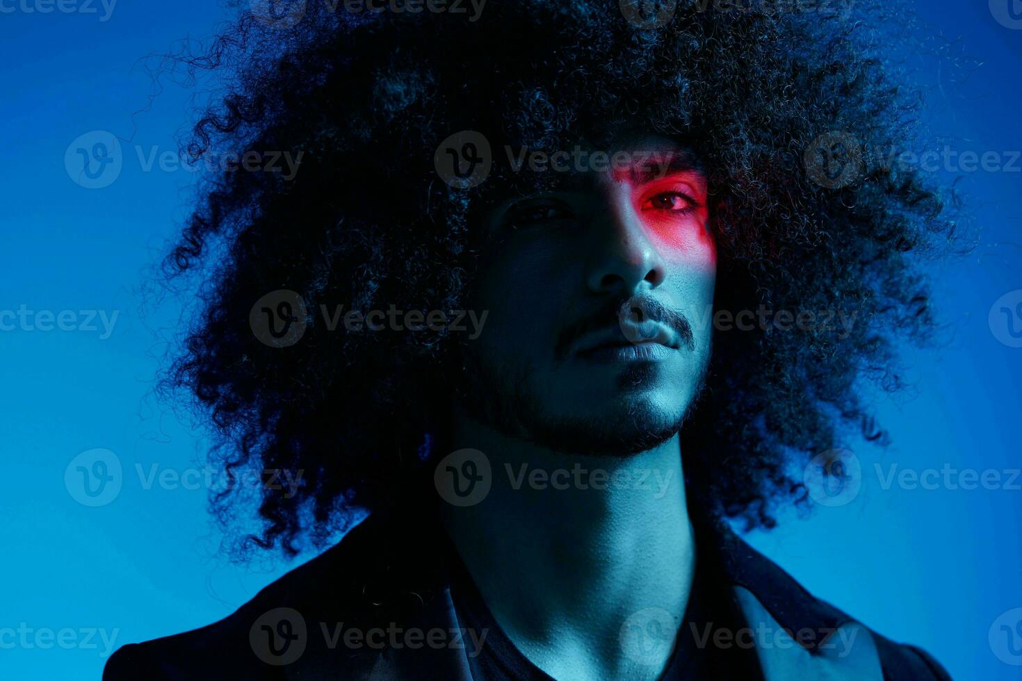 Fashion portrait of a man with curly hair on a blue background with a red stripe of light, multicolored light, trendy, modern concept. photo