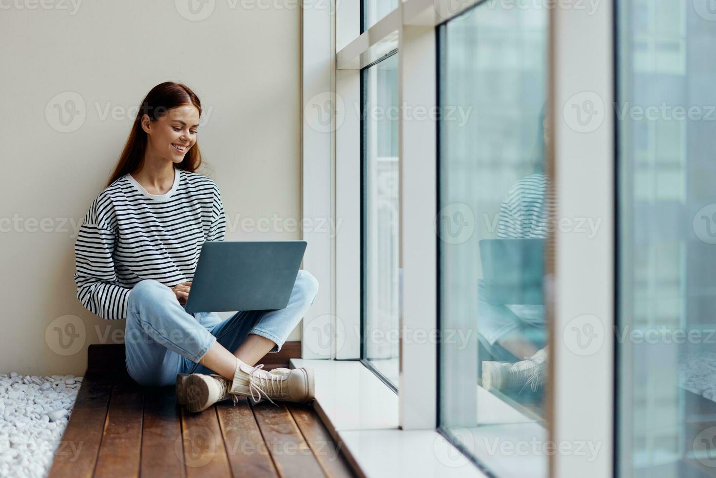 Business woman sitting with a laptop at the window full-length and smiling with teeth and looking out the window, happy woman work online in the office, copy place photo