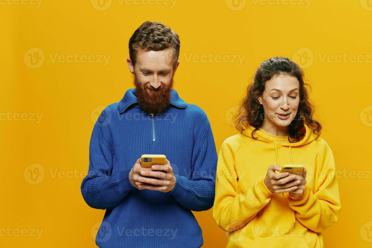 Woman man cheerful couple with phones in hand social networking and communication crooked smile fun and fight, in yellow background. The concept of real family relationships, freelancers, work online. photo