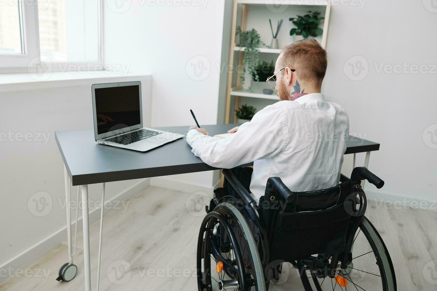 man wheelchair businessman with tattoos in the office works at a laptop online, business process from the back, copy space, integration into society, the concept of working a person with disabilities photo