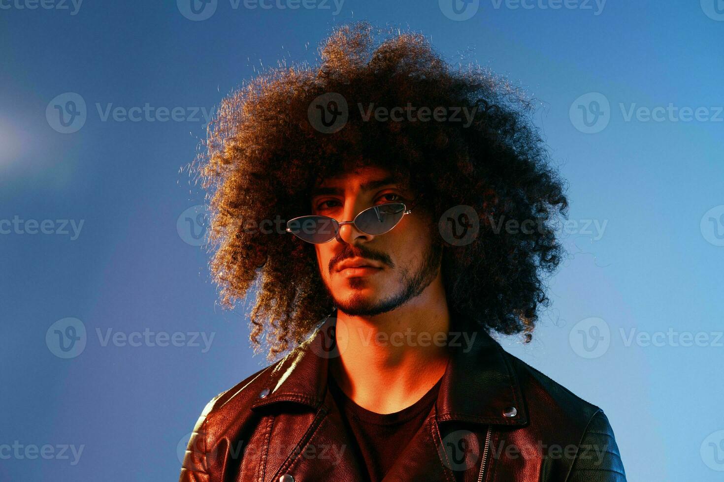Portrait of a stylish man with curly hair on a blue background multinational, colored light, trendy glasses, modern concept. photo