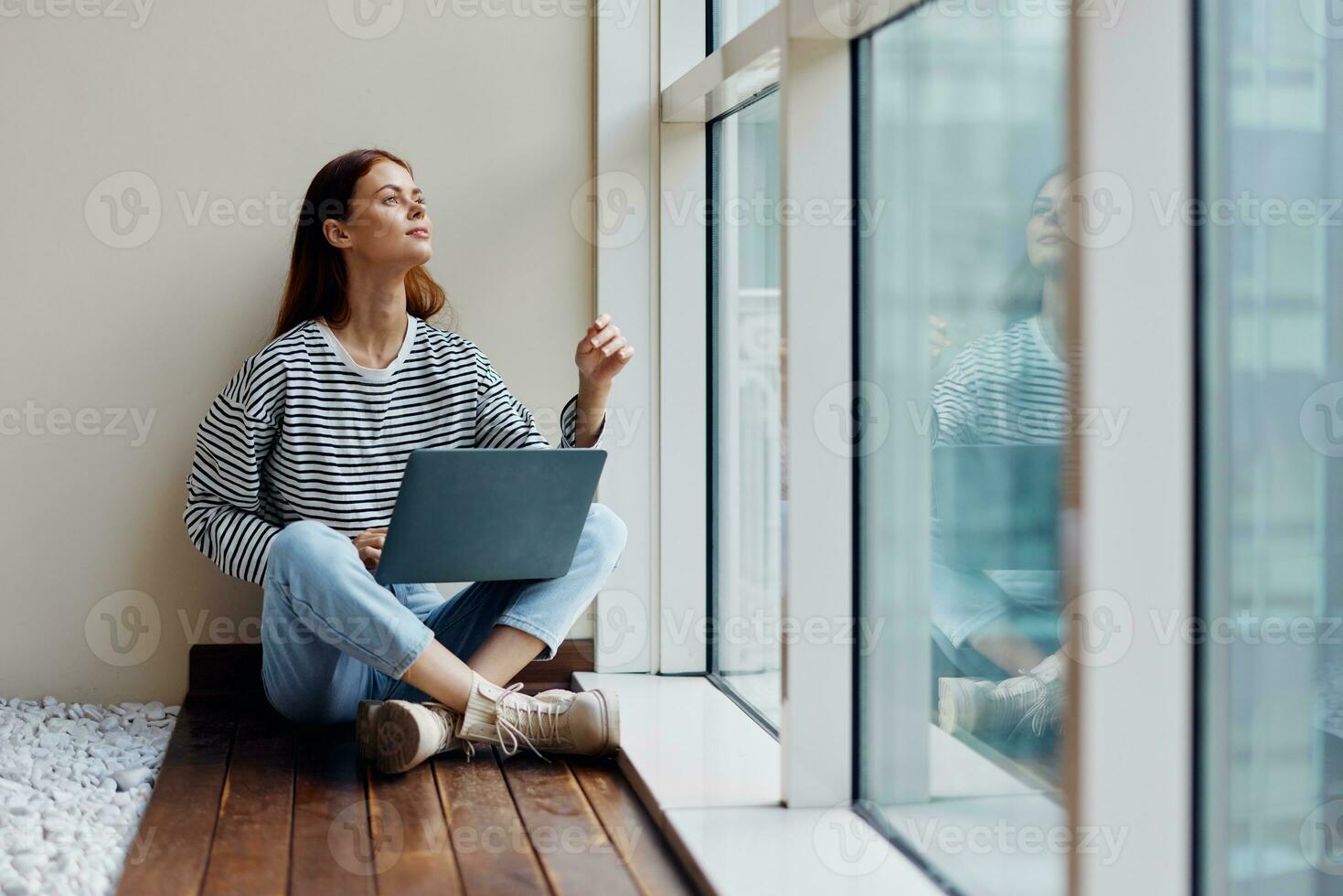 Business woman sitting with a laptop at the window full-length and smiling and looking out the window, happy woman work online in the office, copy space photo