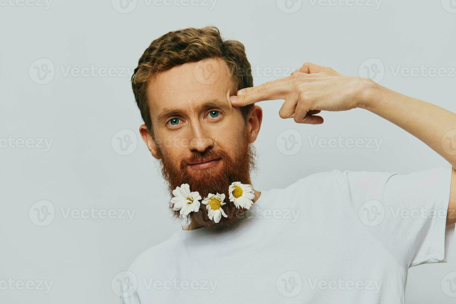 Portrait of a funny man in a white T-shirt with flowers daisies in his beard on a white isolated background, copy place. Holiday concept and congratulations. photo