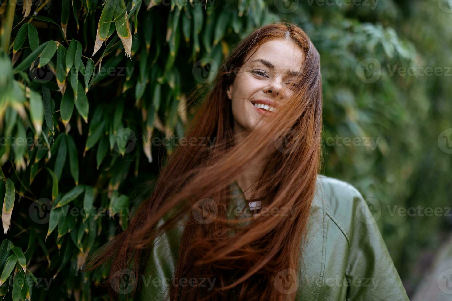 Portrait of happiness woman with red flying hair smile with teeth walking in the city in the park against a backdrop of green bamboo leaves, spring in the city photo