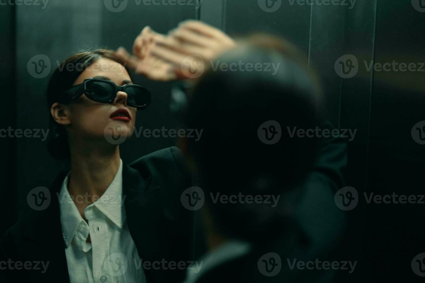 Stylish woman in a black jacket and sunglasses posing in an elevator lift near the mirror, fashion model, dark cinematic light and color matrix, glamor vintage photo