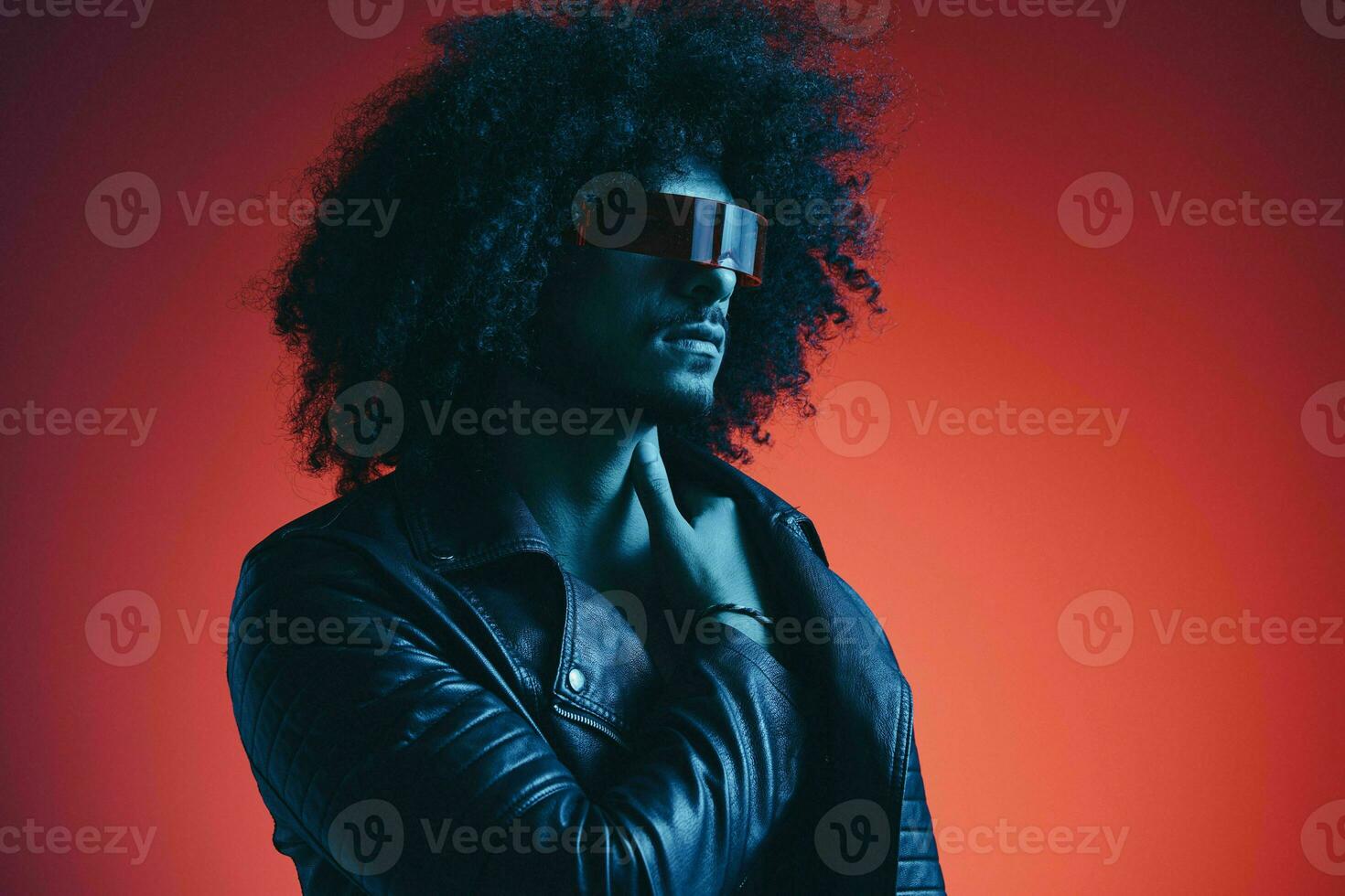 Portrait of fashion man with curly hair on red background with stylish glasses, multicultural, colored light, black leather jacket trend, modern concept. photo
