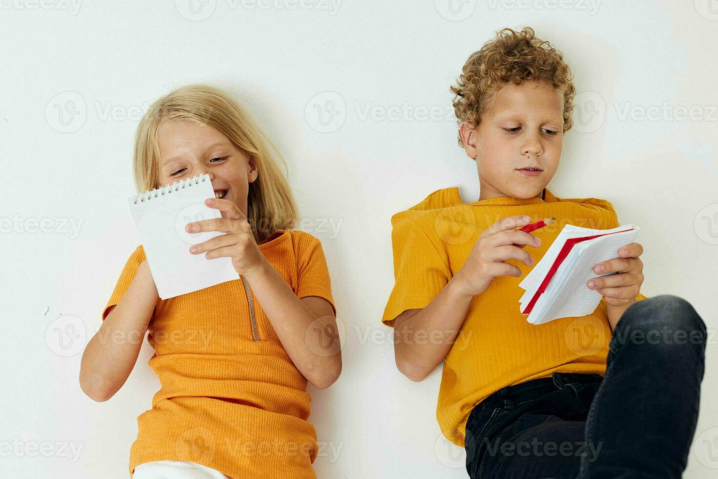 dos alegre niños dibujo en cuadernos acostado en el piso ligero antecedentes inalterado foto