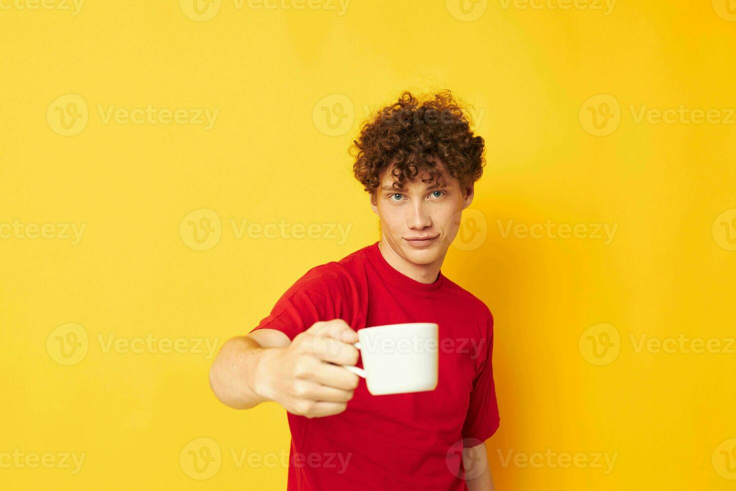 portrait of a young curly man white mug in the hands of a drink yellow background unaltered photo